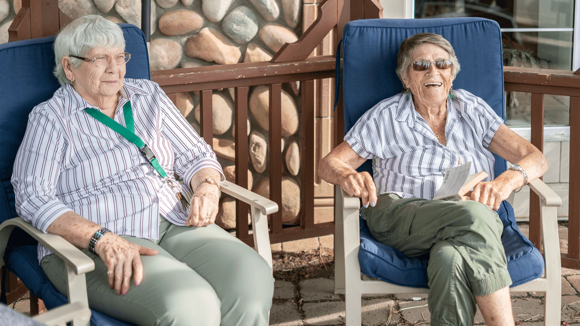 In the patio's shadow, two elderly people are seated and smiling