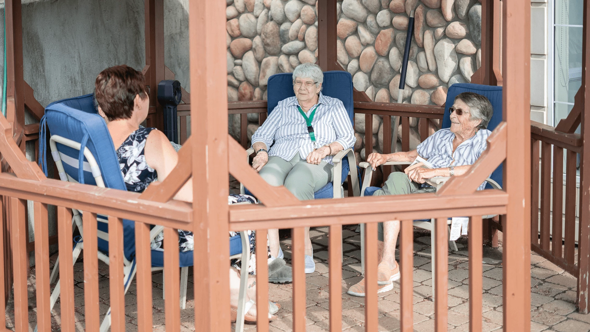 In the patio's shadow, three elderly people are seated and smiling
