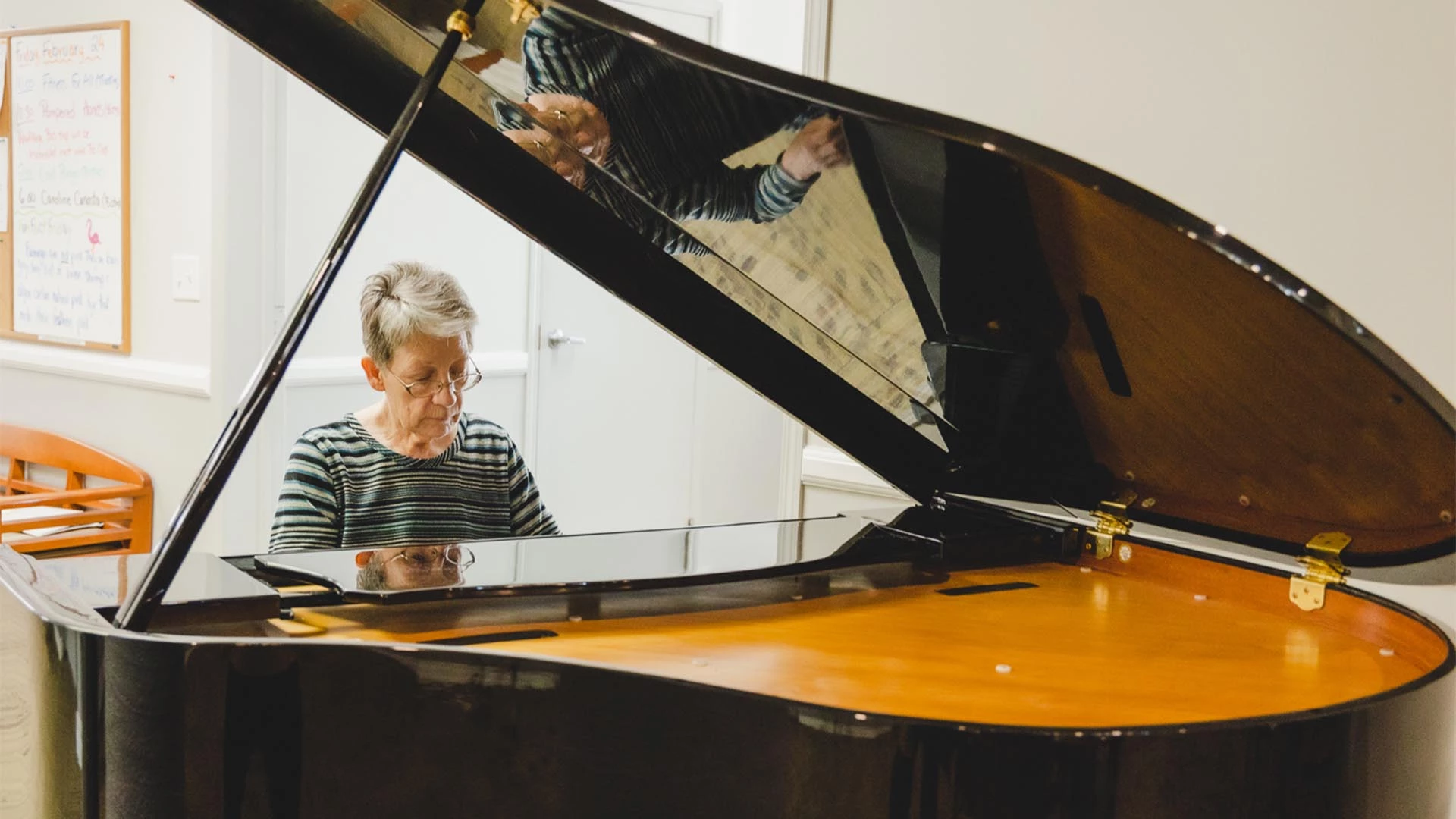 Woman with glasses playing the piano inside her senior apartments